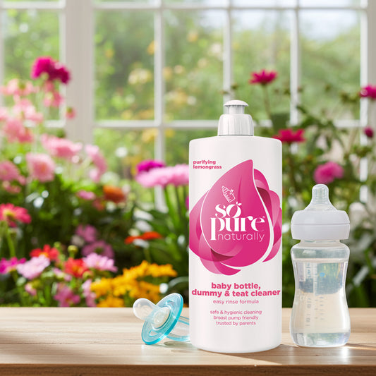 Baby bottle, dummy, and teat cleaner with flowers in the background