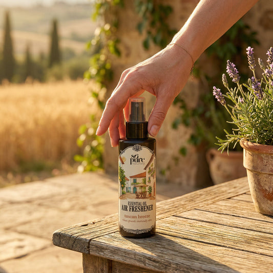 Hand holding a bottle of air freshener outdoors with a scenic background